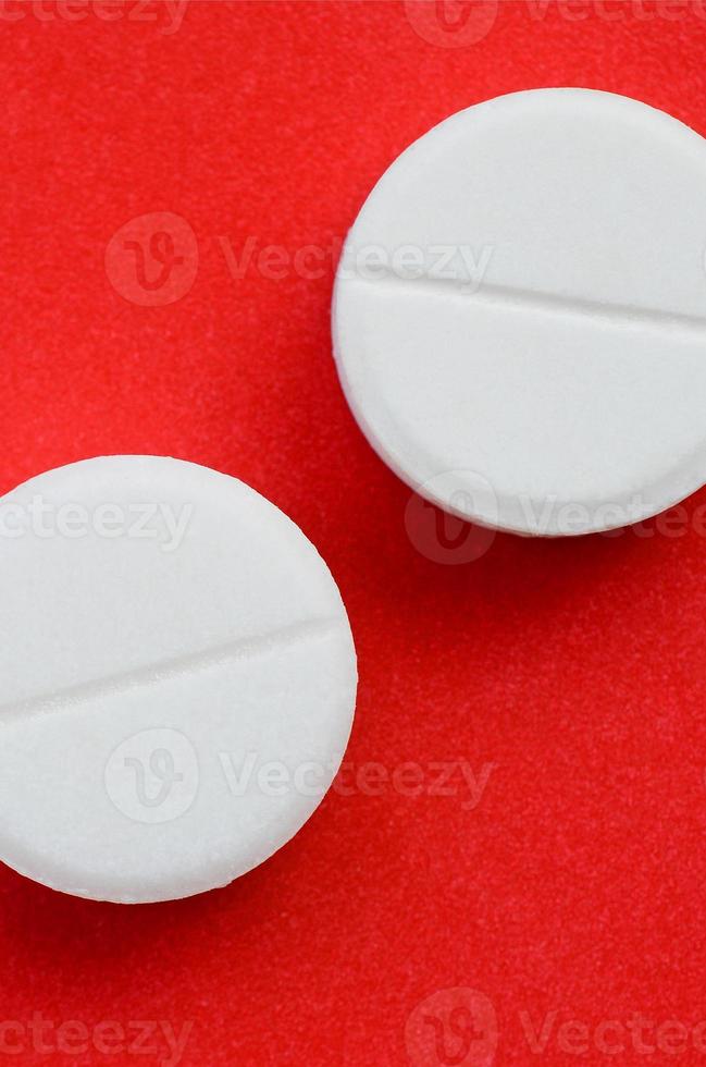 A few white tablets lie on a bright red background surface. Background image on medical and pharmaceutical topics photo