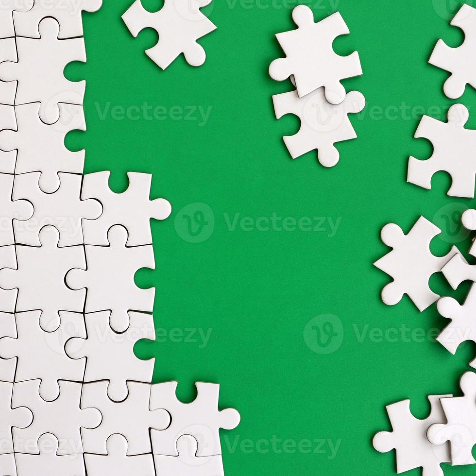 Fragment of a folded white jigsaw puzzle and a pile of uncombed puzzle elements against the background of a green surface. Texture photo with space for text