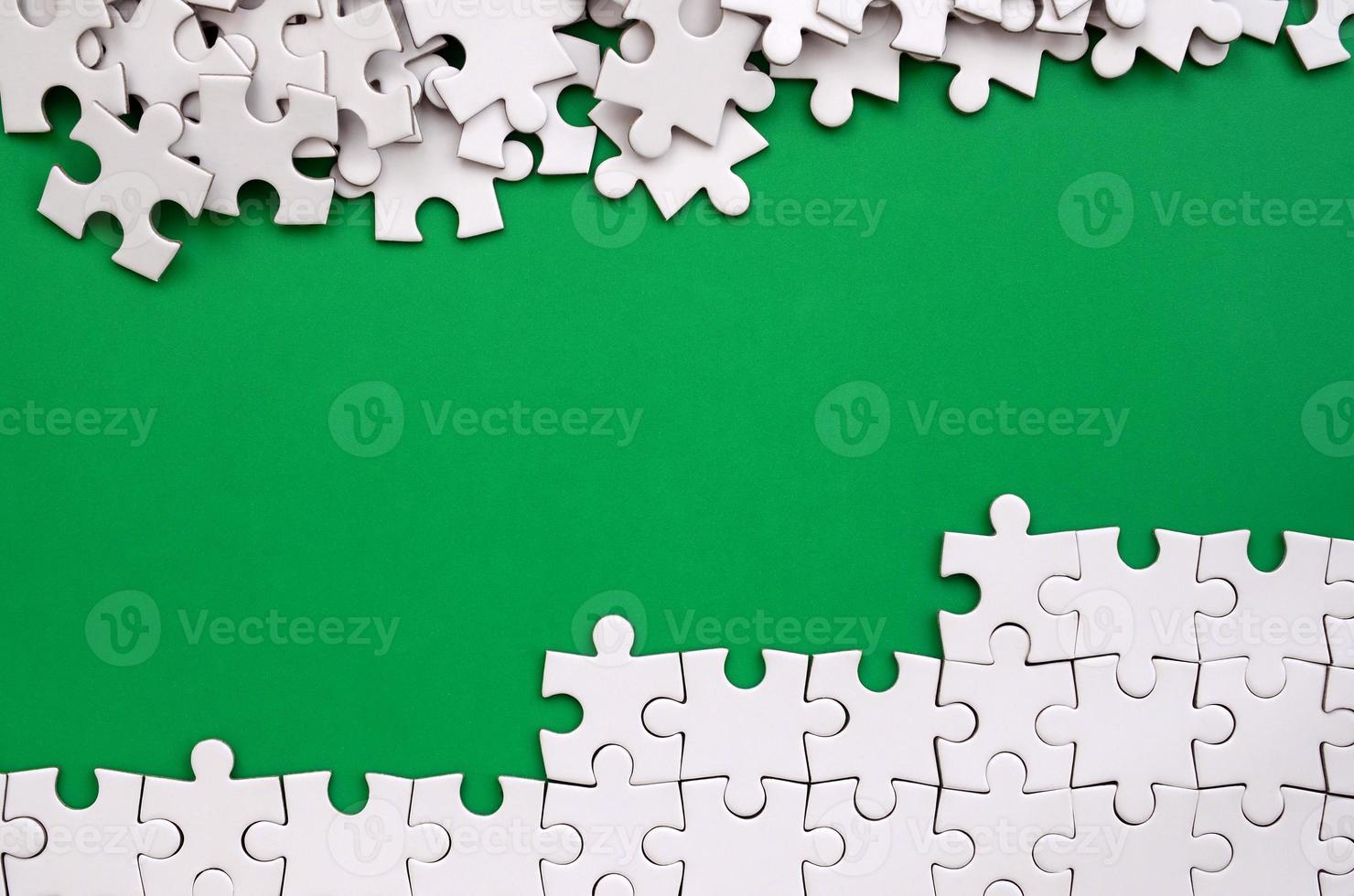 Fragment of a folded white jigsaw puzzle and a pile of uncombed puzzle elements against the background of a green surface. Texture photo with space for text