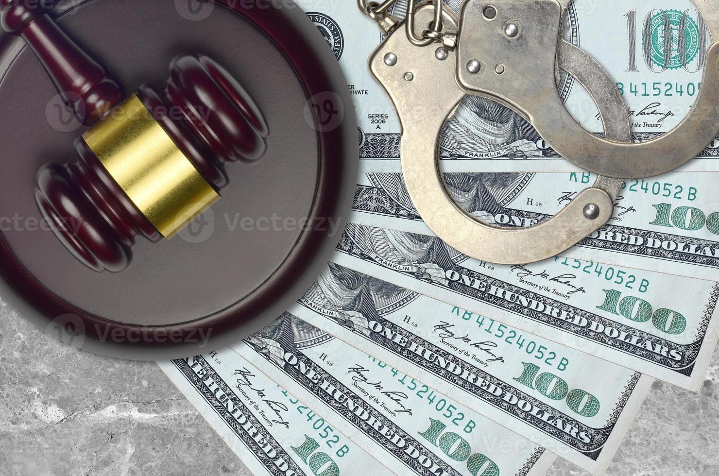 100 US dollars bills and judge hammer with police handcuffs on court desk. Concept of judicial trial or bribery. Tax avoidance photo