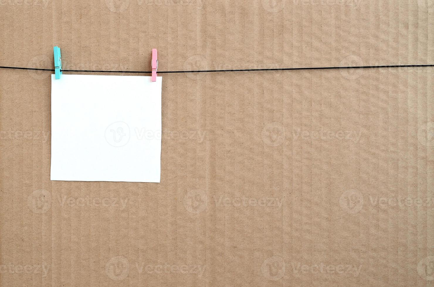 White blank card on rope on a brown cardboard background. Creative reminder, small sheet of paper on wooden clothespin, memo backdrop photo