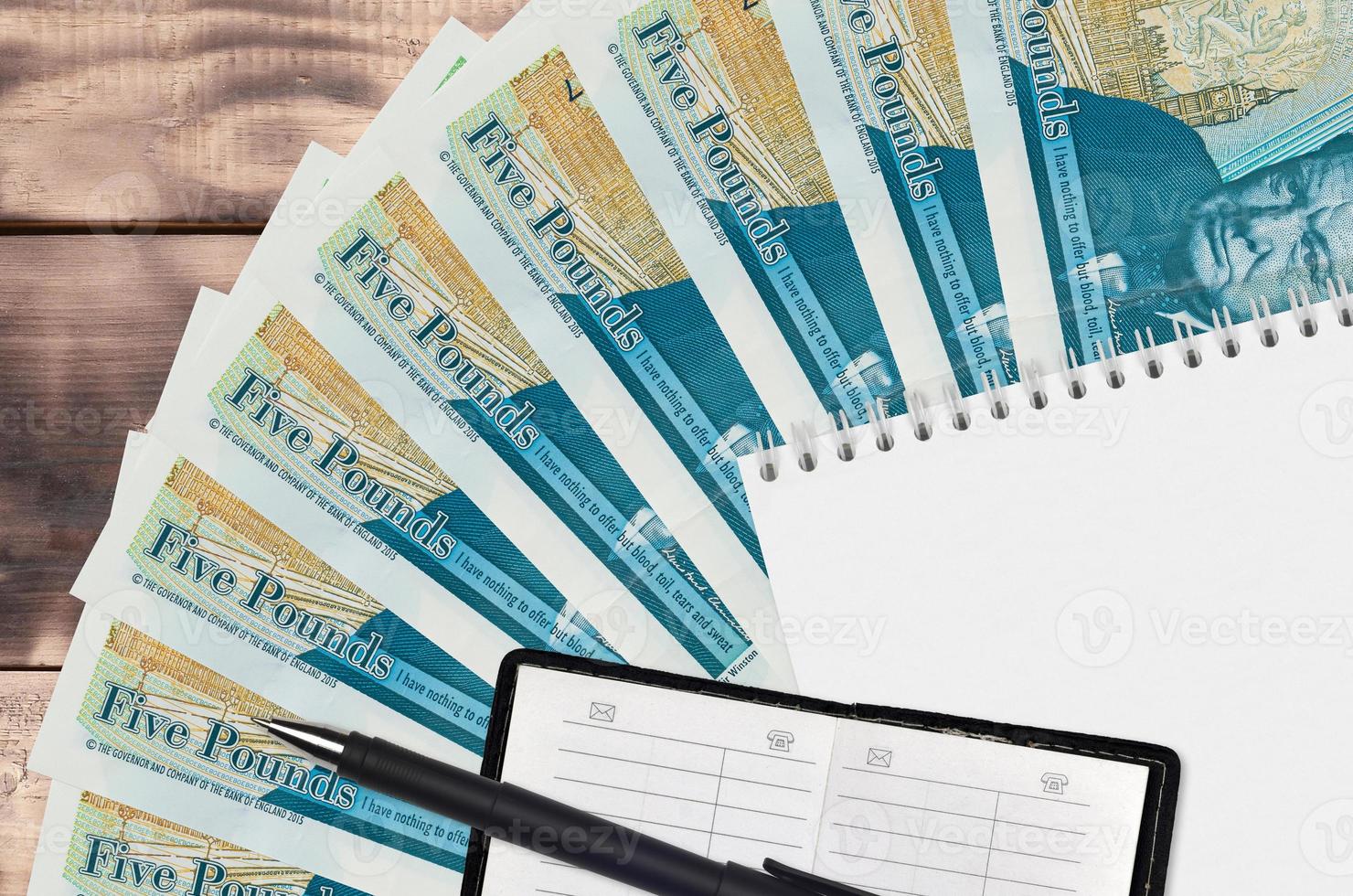 5 British pounds bills fan and notepad with contact book and black pen. Concept of financial planning and business strategy photo