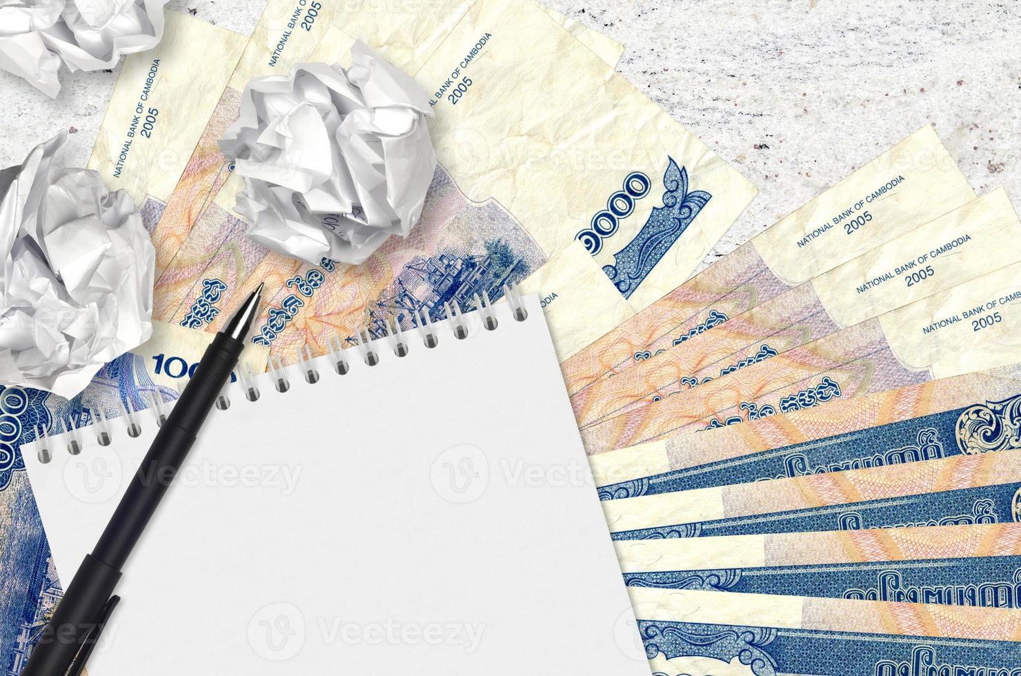 1000 Cambodian riels bills and balls of crumpled paper with blank notepad. Bad ideas or less of inspiration concept. Searching ideas for investment photo