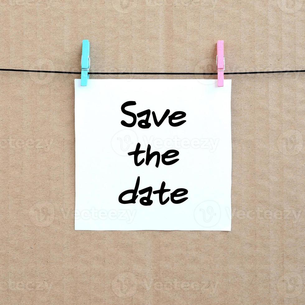 Save the date. Note is written on a white sticker that hangs with a clothespin on a rope on a background of brown cardboard photo