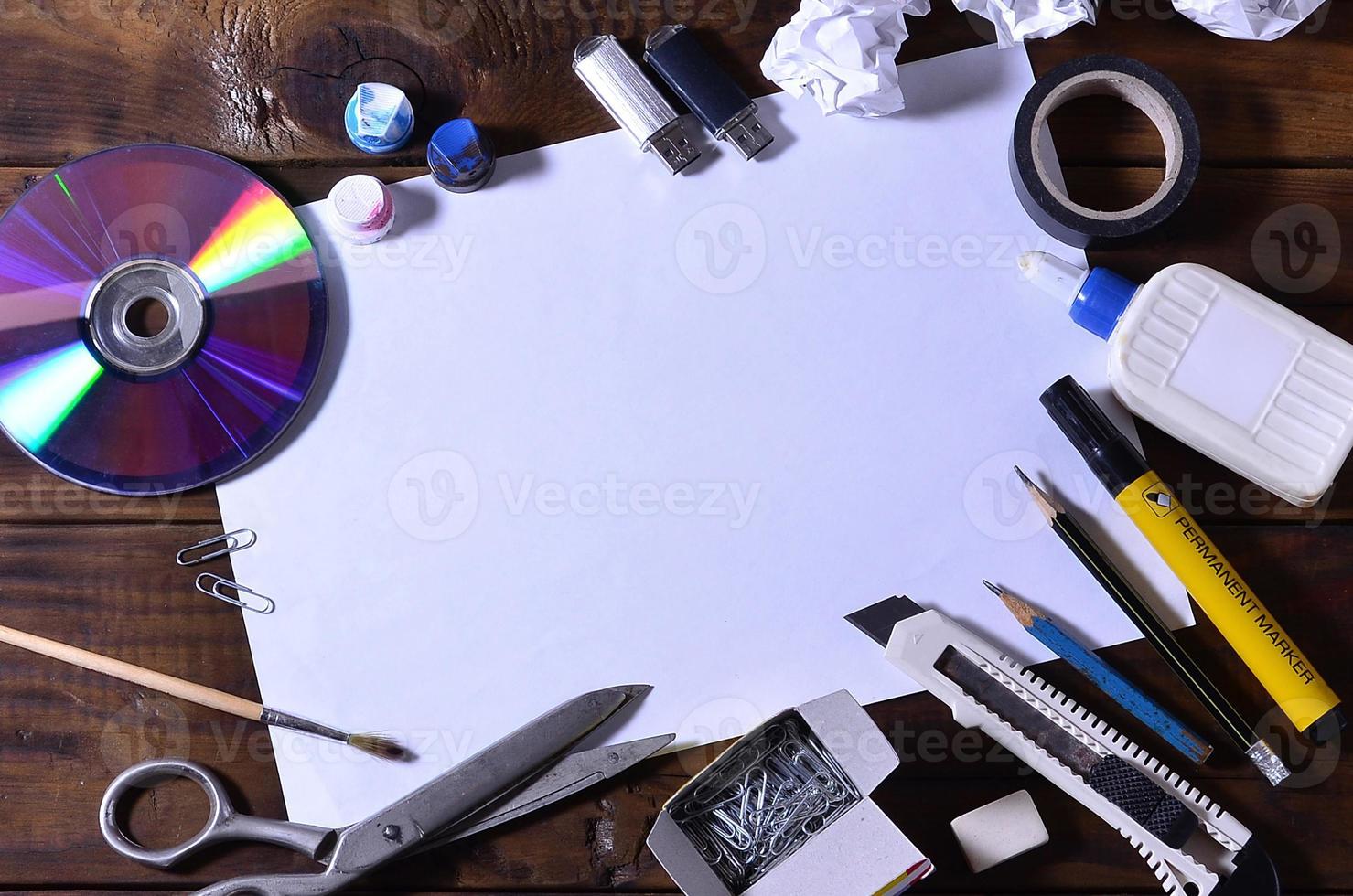 A school or office still life with a white blank sheet of paper and many office supplies. The school supplies lie on a brown wooden background. Place for text photo