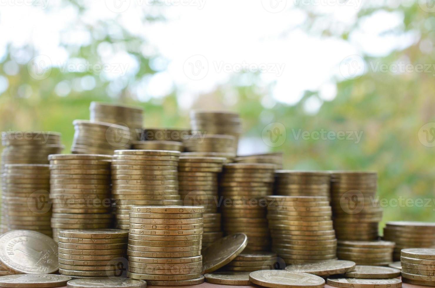 Big amount of shiny ukrainian old 1 hryvnia coin stacks close up on wooden table on green trees backdrop. The concept of business and rich life in Ukraine photo