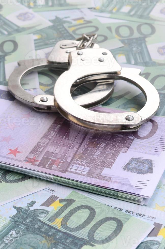 Police handcuffs lies on a set of green monetary denominations of 100 euros. A lot of money forms an infinite heap photo
