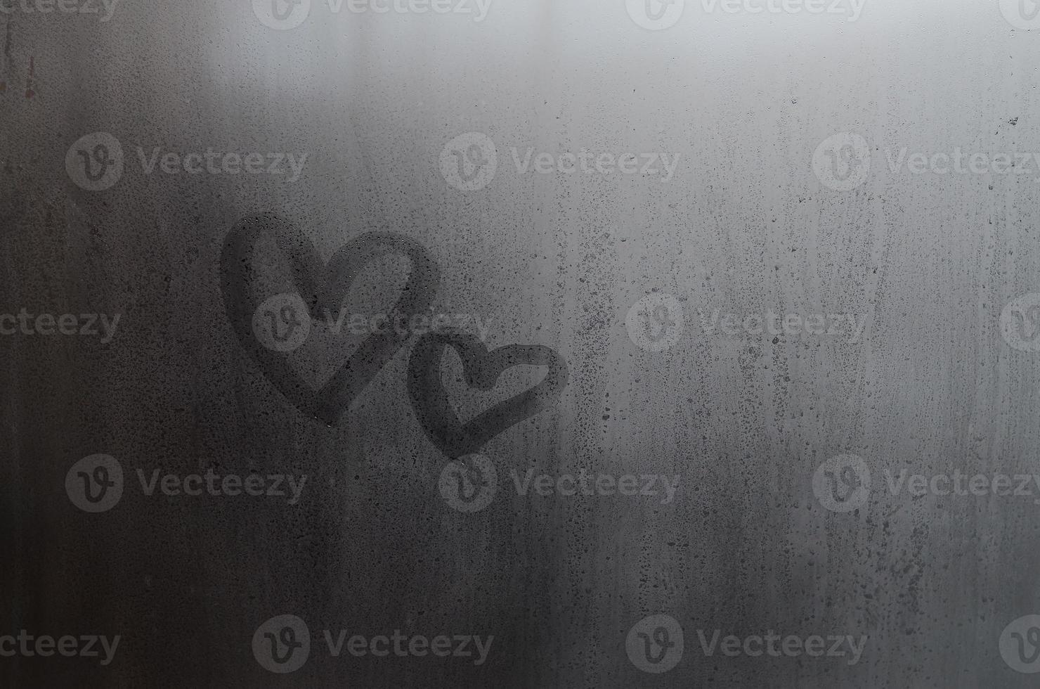 Couple of abstract blurred love heart symbol drawn by hand on the wet window glass with sunlight background. Template for Valentine Day postcards photo