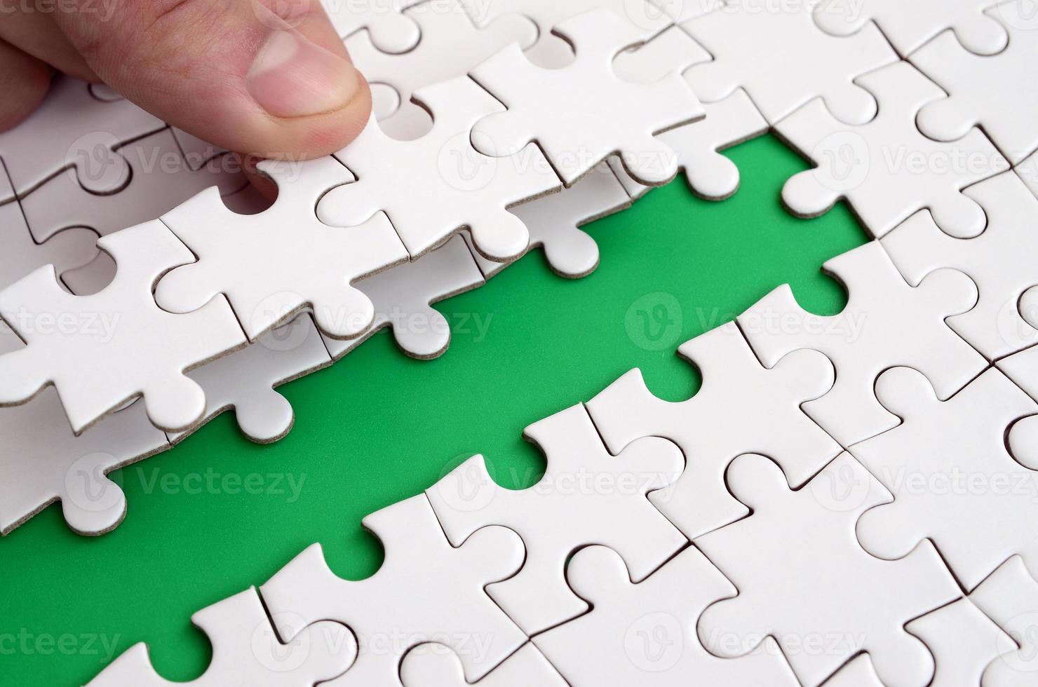 The human hand paves the way to the surface of the jigsaw puzzle, forming a green space. The concept of overcoming the difficulties on the way to success photo