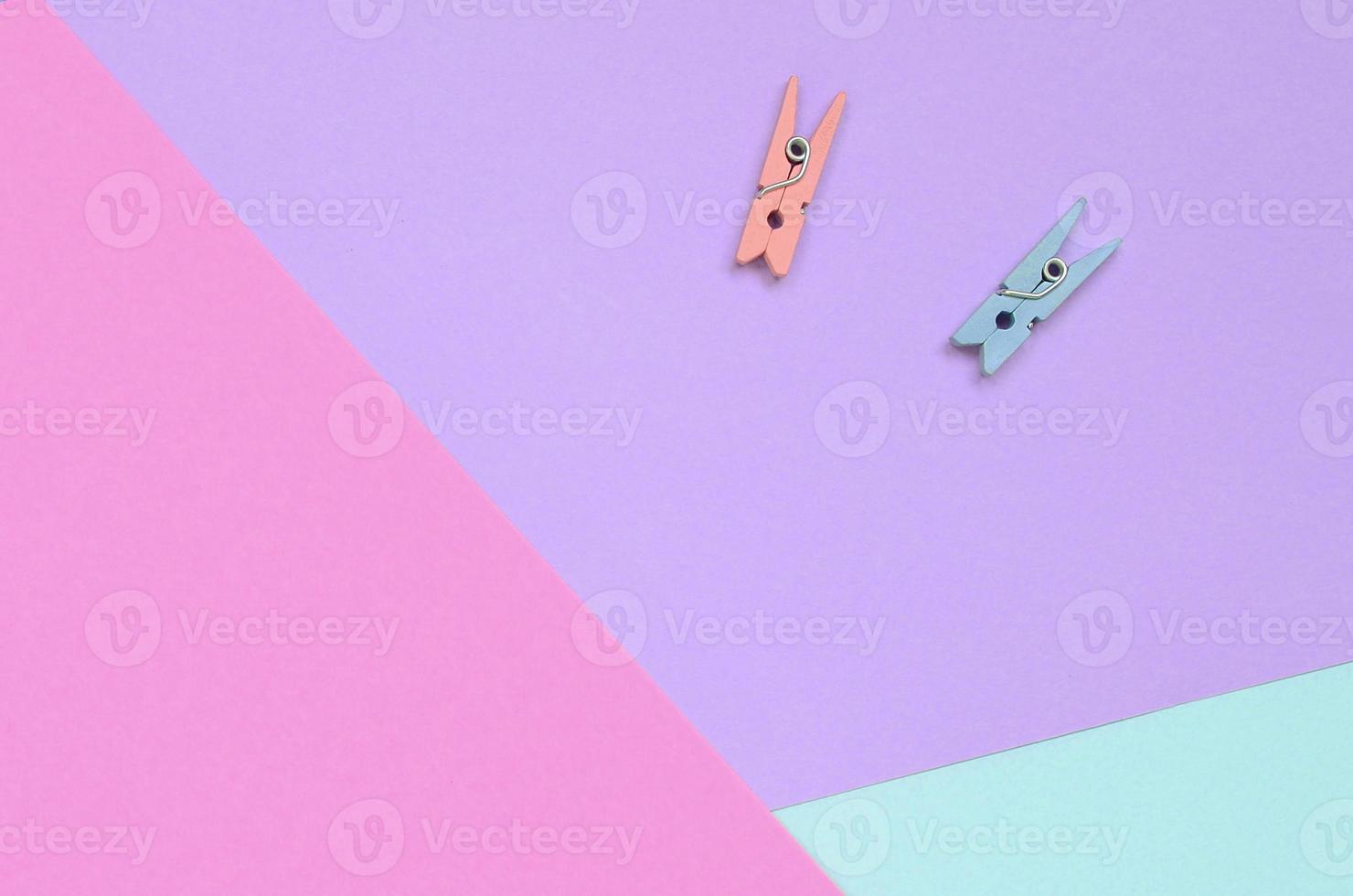 Two colored wooden pegs lie on texture background of fashion pastel violet, blue and pink colors paper in minimal concept photo