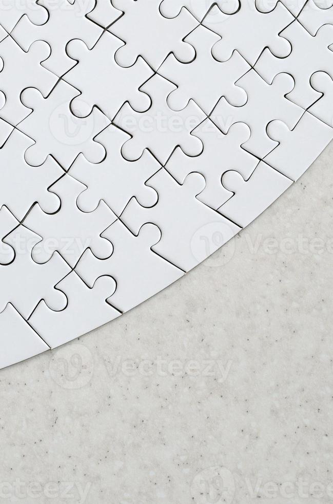 A white jigsaw puzzle in the complete form lies on a treated stone surface. Textured image with copy space photo