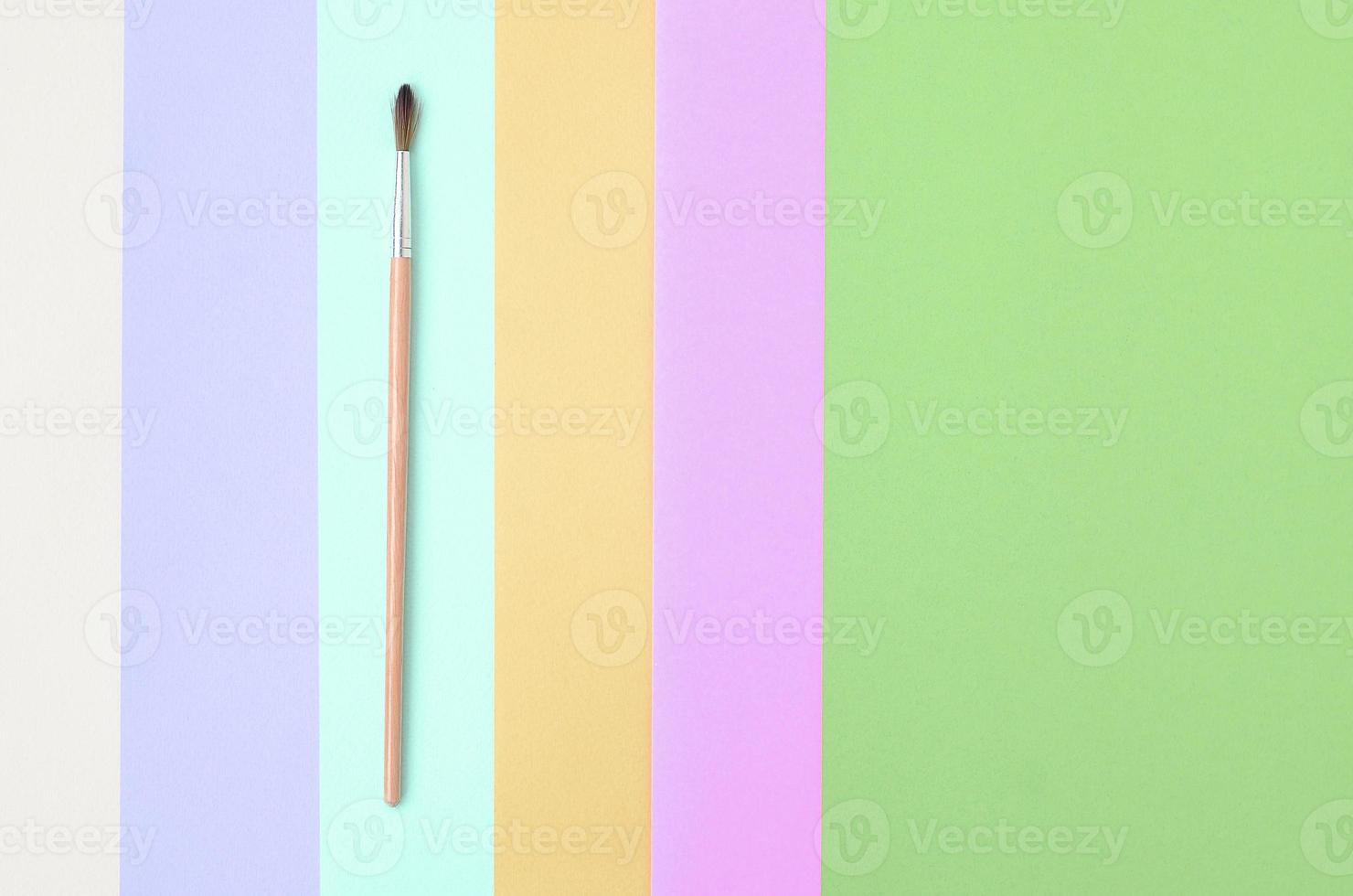 A new paint brush lie on texture background of fashion pastel pink, blue, green, yellow, violet and beige colors paper photo
