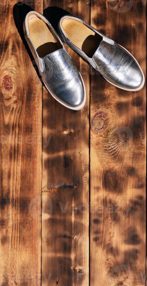 Original shiny shoes in disco style lie on a vintage wooden surface made from fried brown boards. Fashionable clothing retro accessory for discos and parties in the style of the eighties photo