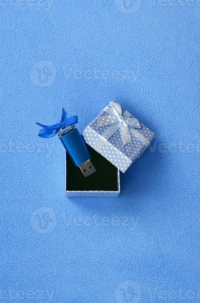 Brilliant blue usb flash memory card with a blue bow lies in a small gift box in blue with a small bow on a blanket of soft and furry light blue fleece fabric. Classic female gift memory card design photo