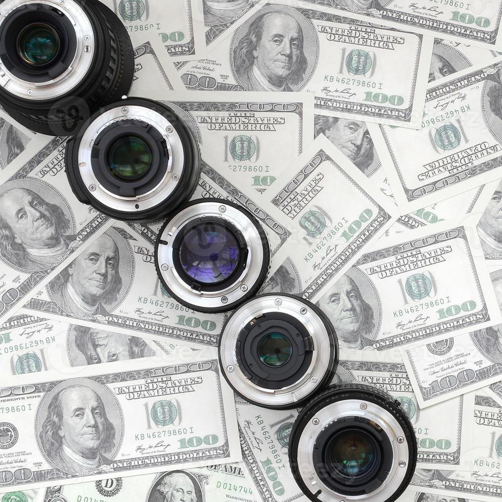 A few photographic lenses lies on the background of a lot of dollar bills. Space for text photo