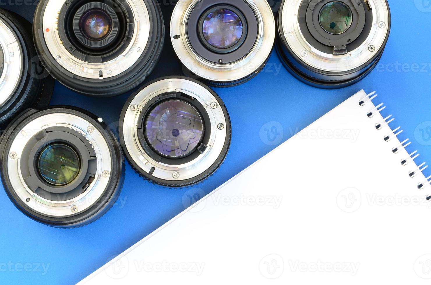 Several photographic lenses and white notebook lie on a bright blue background. Space for text photo