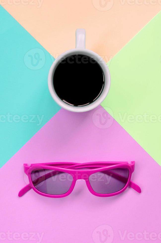 Small white coffee cup and pink sunglasses on background of fashion pastel pink, blue, coral and lime colors photo