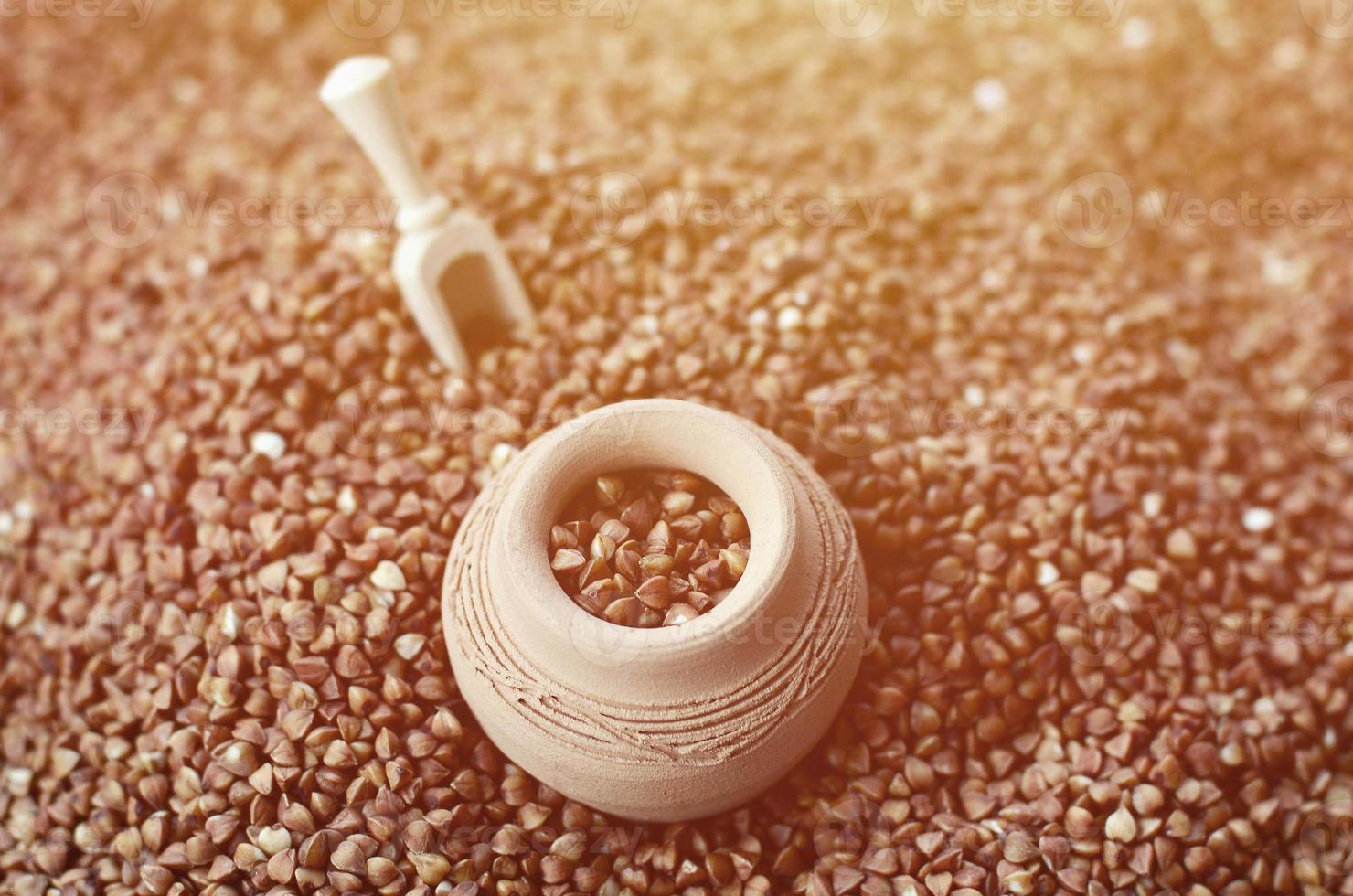 Background image of a large pile of buckwheat, in the middle of which lies a small jug and a wooden spatula for cereals photo