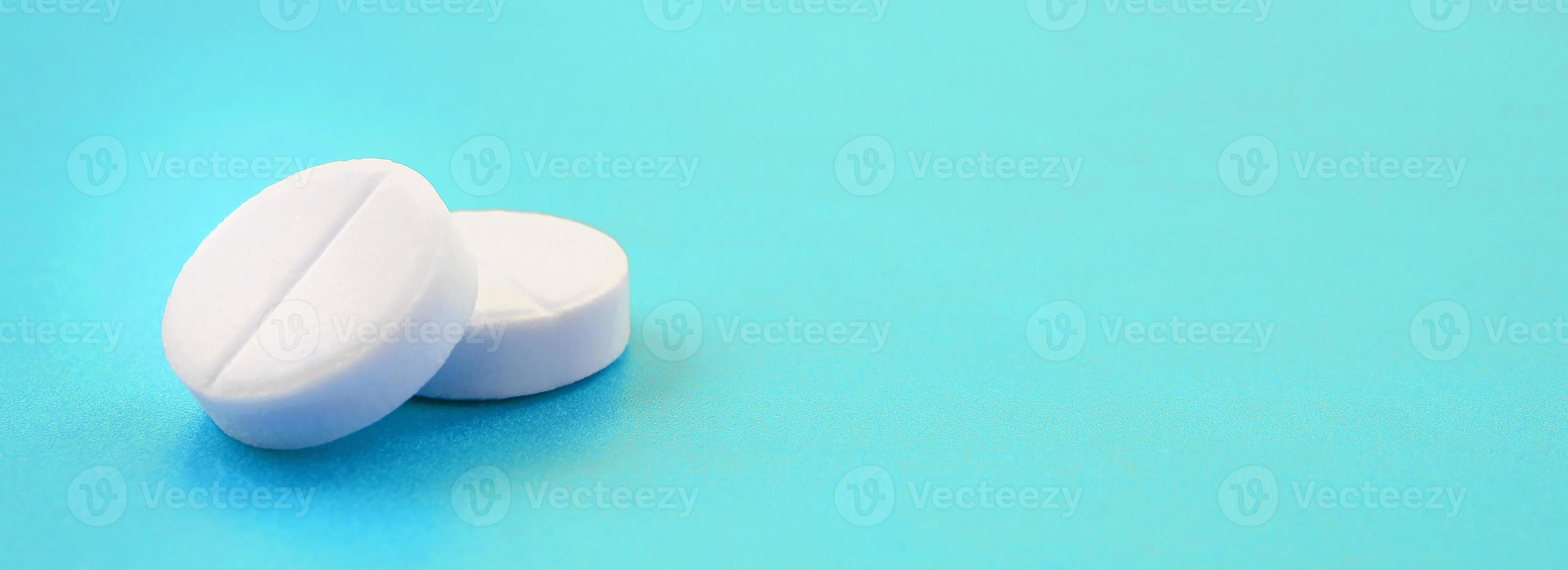 A few white tablets lie on a bright blue background surface. Background image on medical and pharmaceutical topics photo