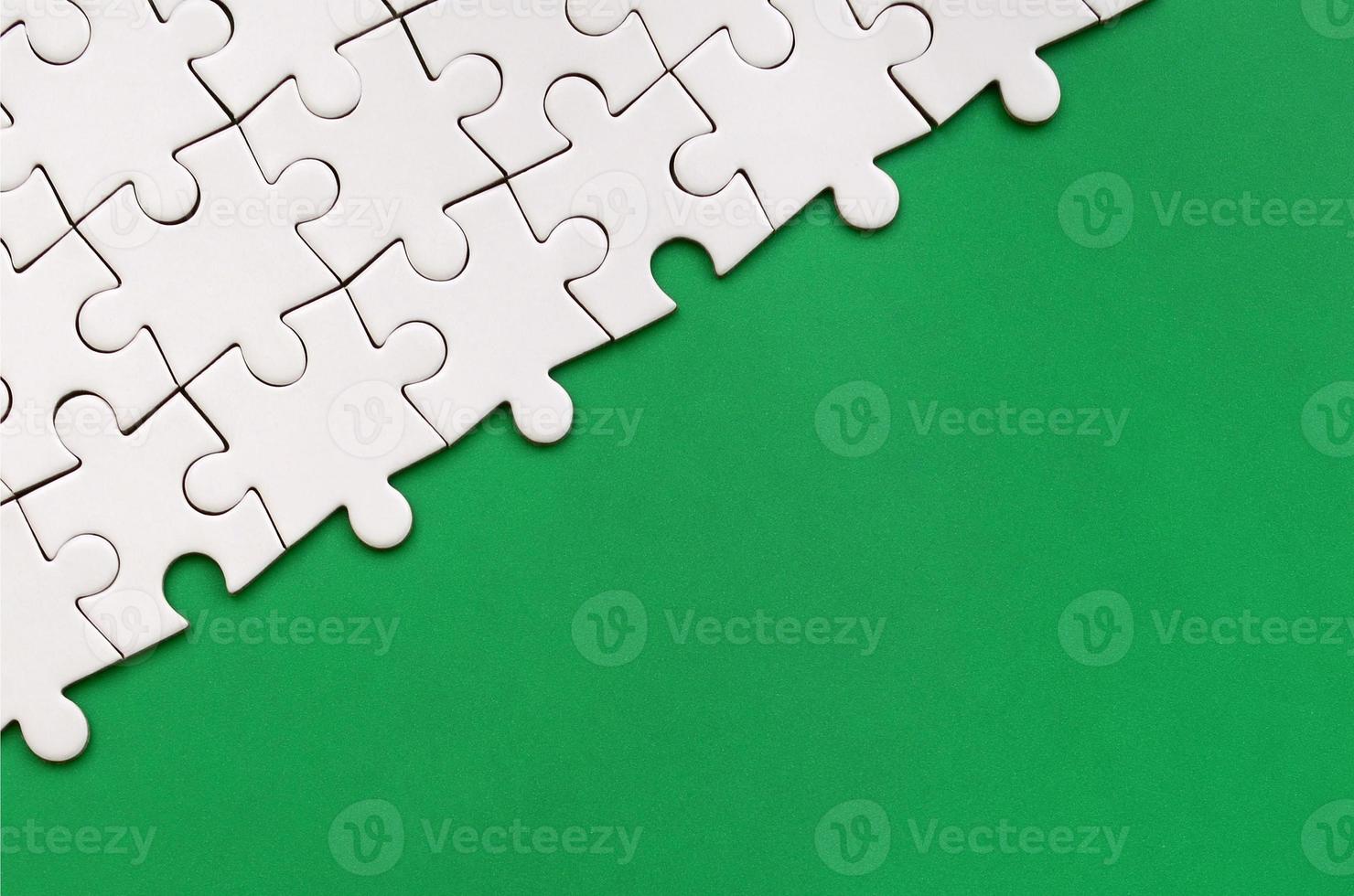 Fragment of a folded white jigsaw puzzle on the background of a green plastic surface. Texture photo with copy space for text