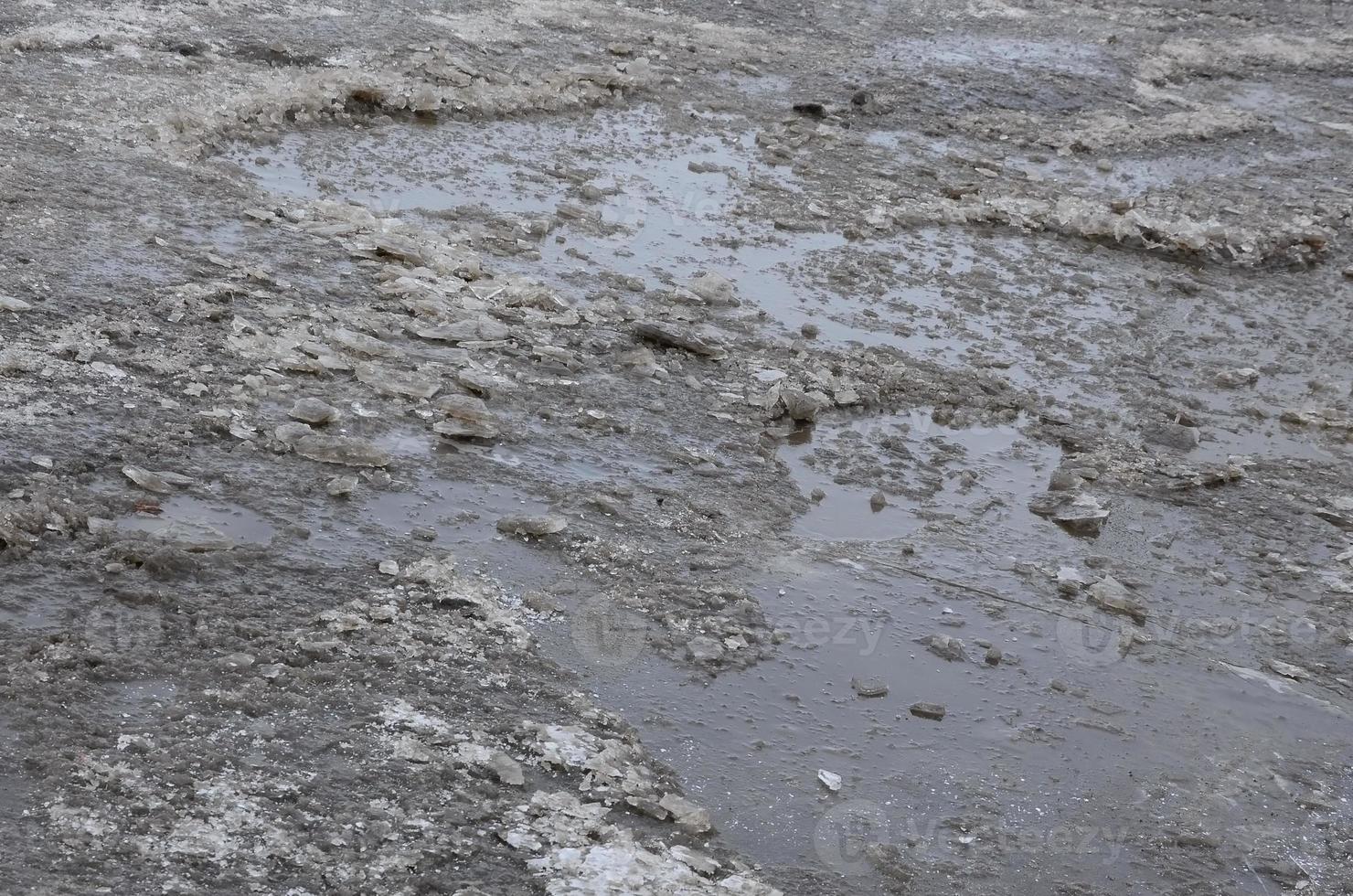 Damaged asphalt road with potholes caused by freezing and thawing cycles during the winter. Poor road photo