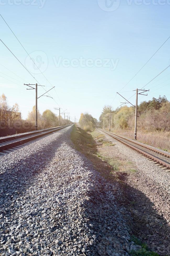 Autumn industrial landscape. Railway receding into the distance among green and yellow autumn trees photo