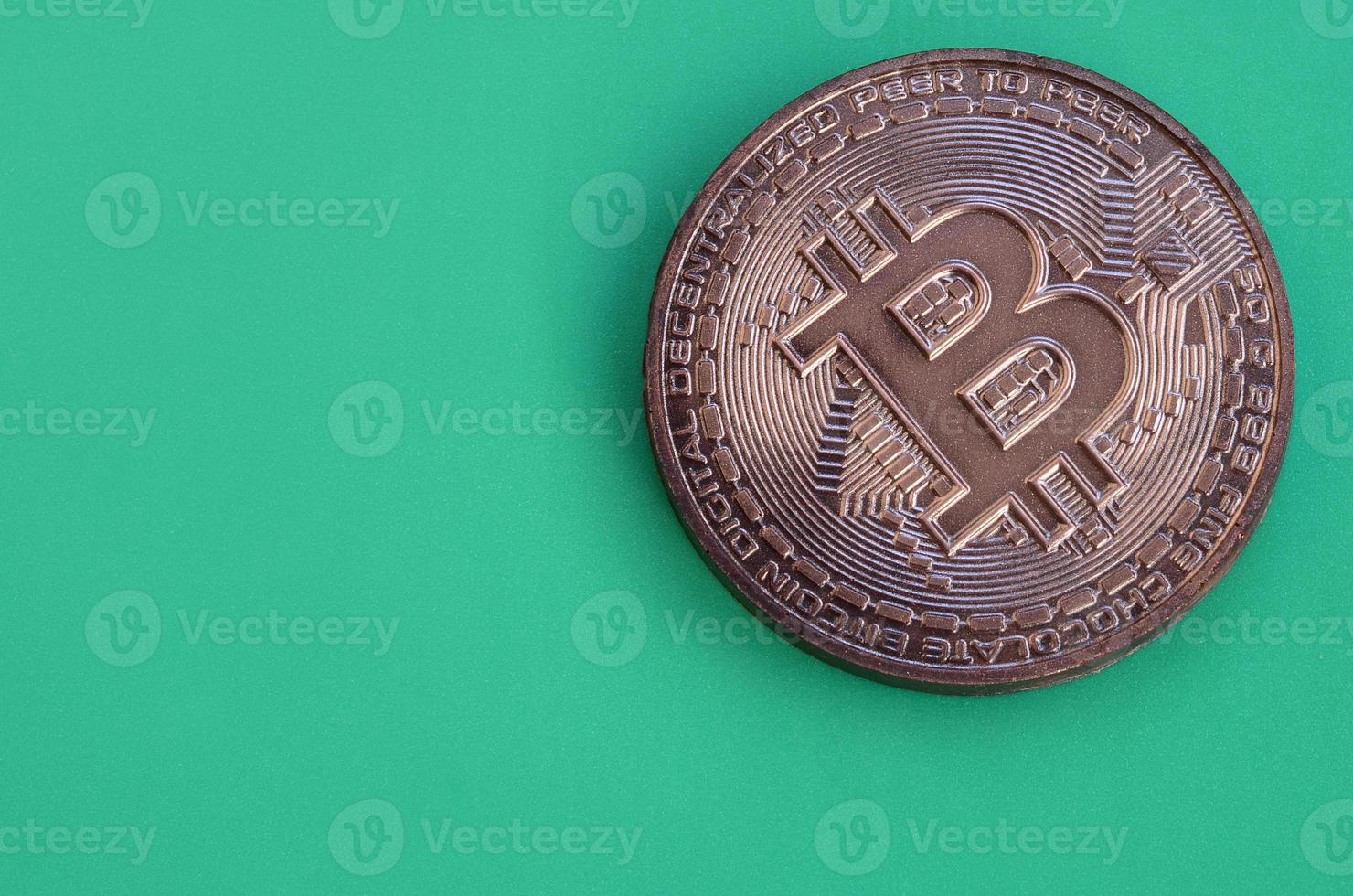 Chocolate product in the form of physical bitcoin lies on a green plastic background. Model of the crypto currency in the edible form photo