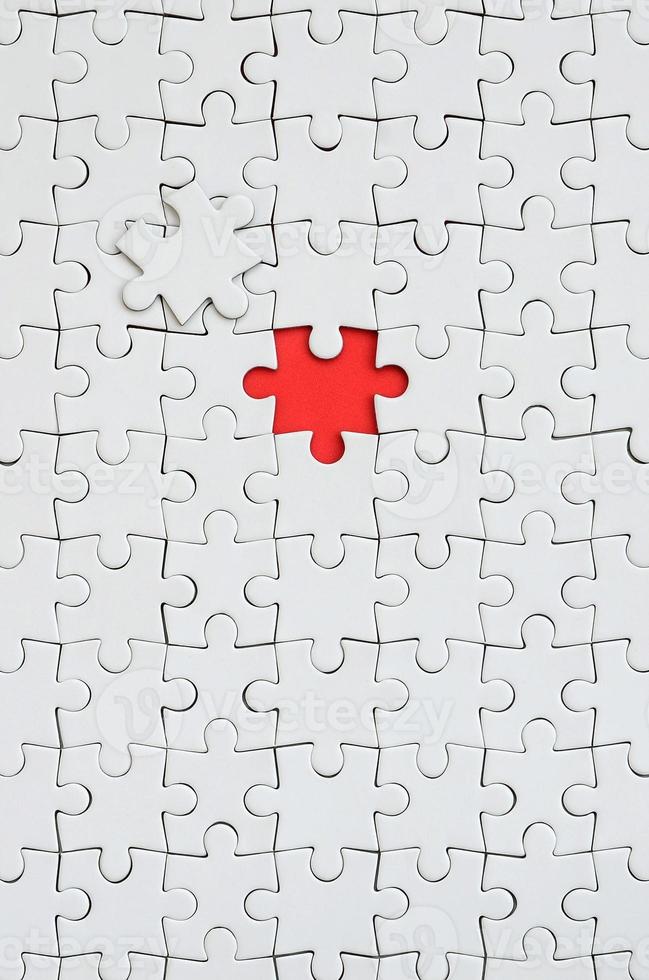 The texture of a white jigsaw puzzle in an assembled state with one missing element forming a red space photo