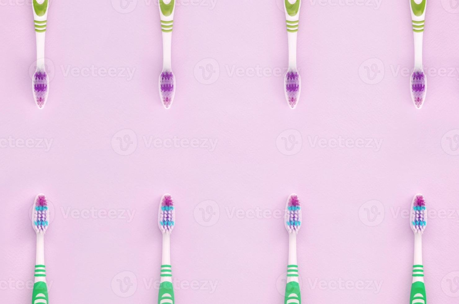 A lot of toothbrushes lie on a pastel pink background photo