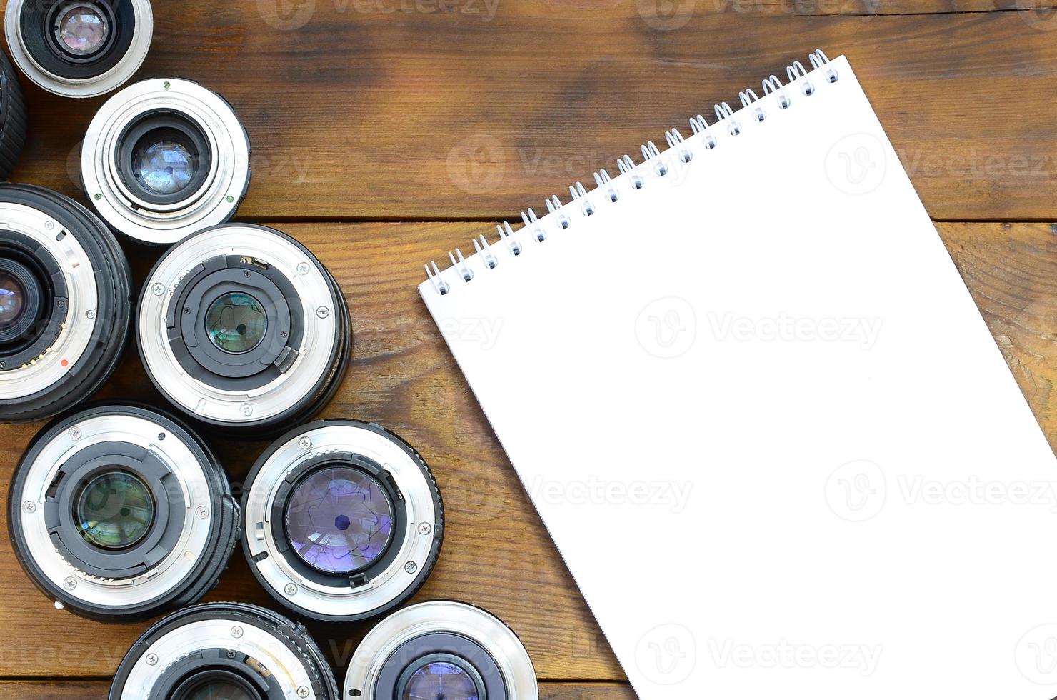 Several photographic lenses and white notebook lie on a brown wooden background. Space for text photo