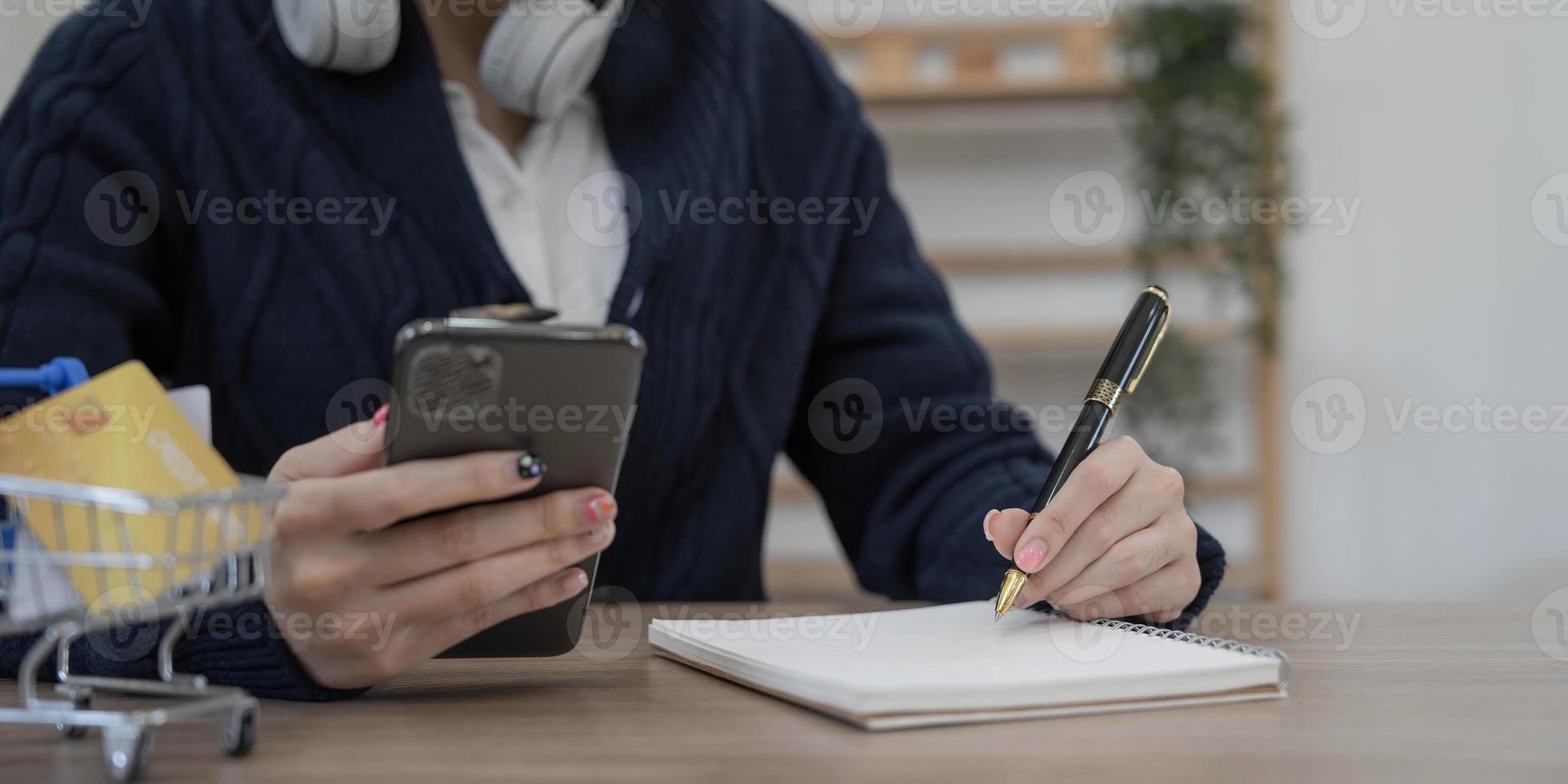 las mujeres usan teléfonos móviles y toman notas en sus cuadernos mientras trabajan en computadoras portátiles, negocios en línea, trabajo desde casa, concepto de teletrabajo. foto