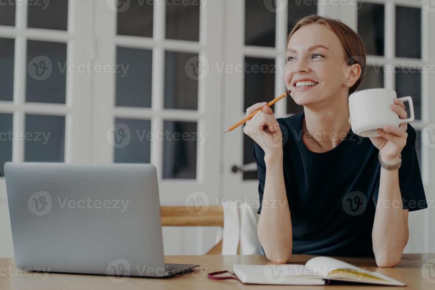 Smiling woman write notes in notebook, sitting at desk, thinking, planning day, visualizing dreams photo