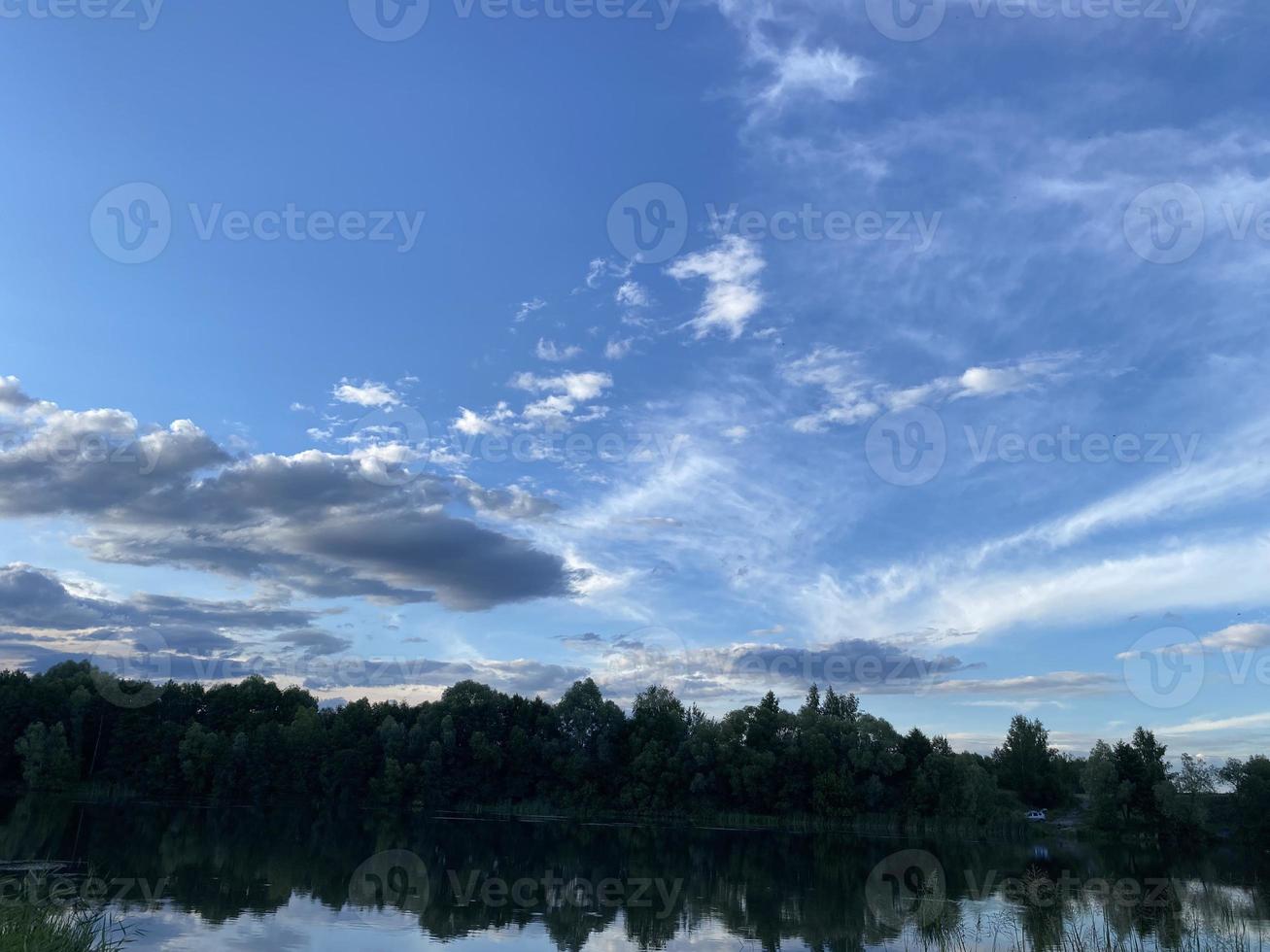 Beautiful sunset on the lake. Sunset reflected in the water - blue and orange sky with clouds and trees in silhouette photo