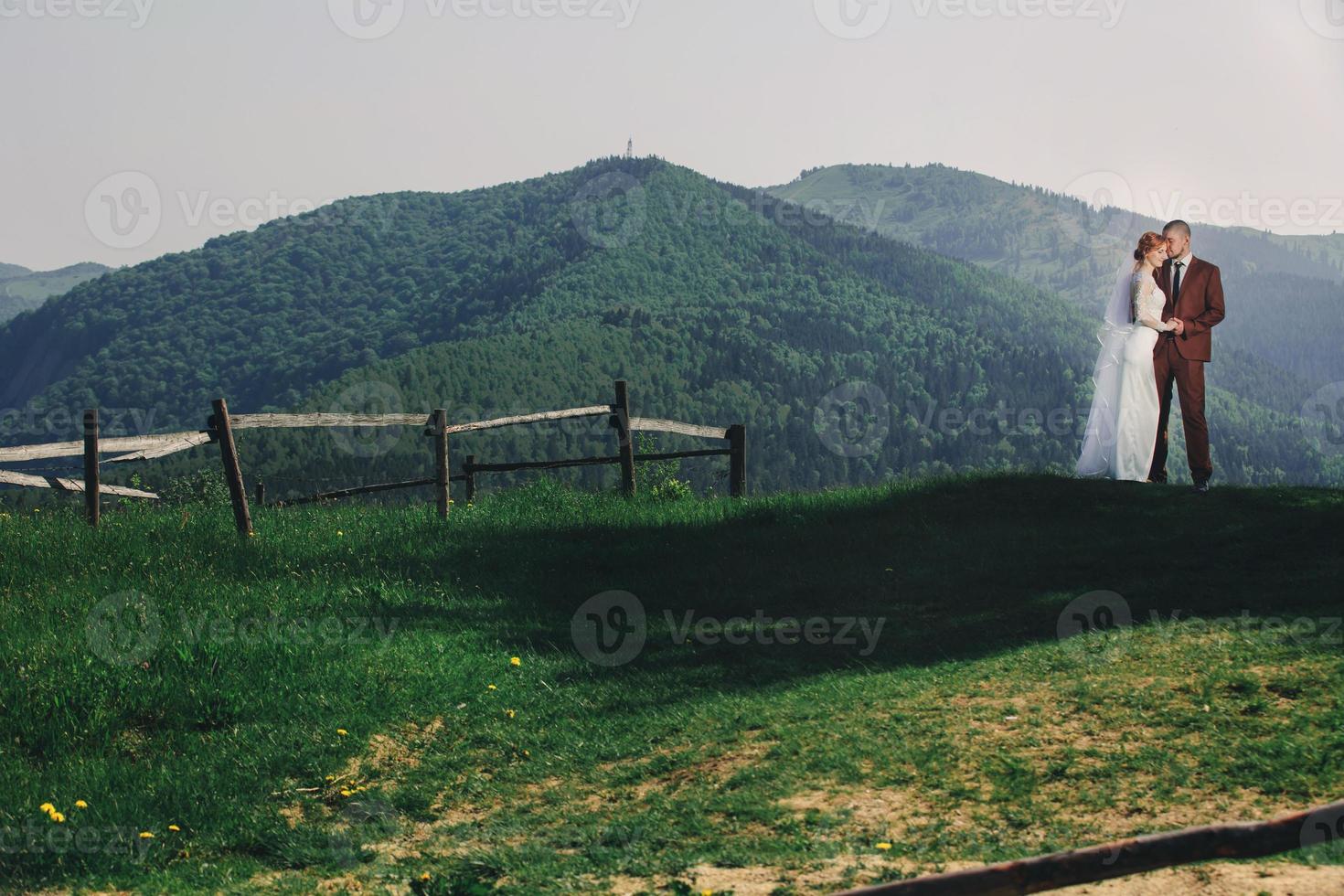 happy stylish bride and groom running and having fun in mountains on summer sunny day. gorgeous newlywed couple laughing, true feelings. emotional romantic moment. photo