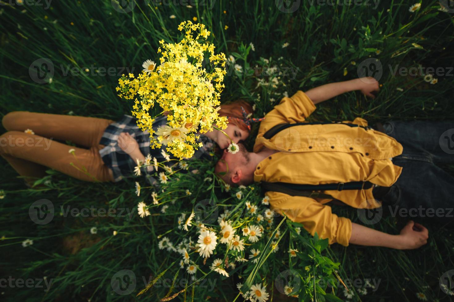 feliz pareja joven hombre y mujer pelirroja recostados sobre hierba verde brillante en el día de verano, vista superior. historia de amor. foto