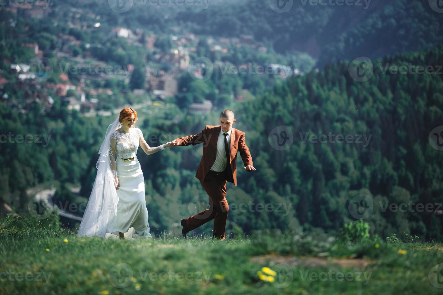 happy stylish bride and groom running and having fun in mountains on summer sunny day. gorgeous newlywed couple laughing, true feelings. emotional romantic moment. photo