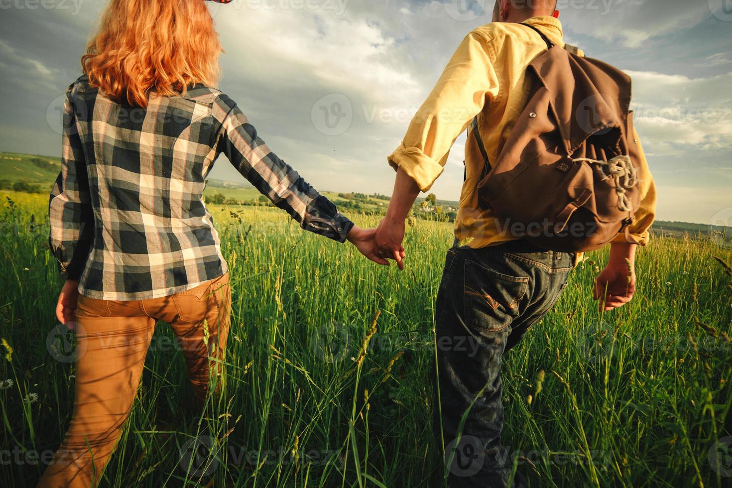 amorosa pareja hipster caminando en el campo, besándose y tomándose de la mano, abrazándose, tumbada en la hierba en el verano al atardecer. día de San Valentín foto