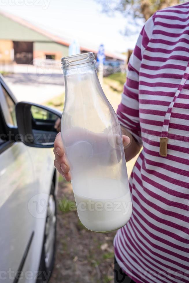 la mano sostiene una botella de leche cruda de la granja, que está casi borracha, contra el fondo de un granero foto