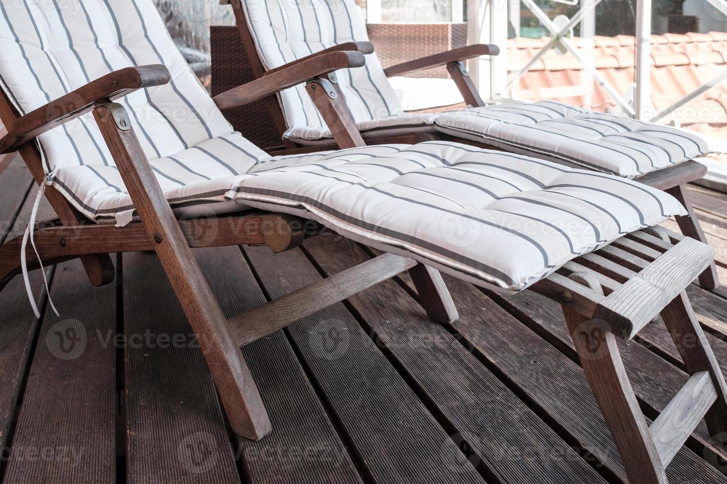 Empty wooden deck chair with a soft pillow on the terrace, against the background of the roofs. photo