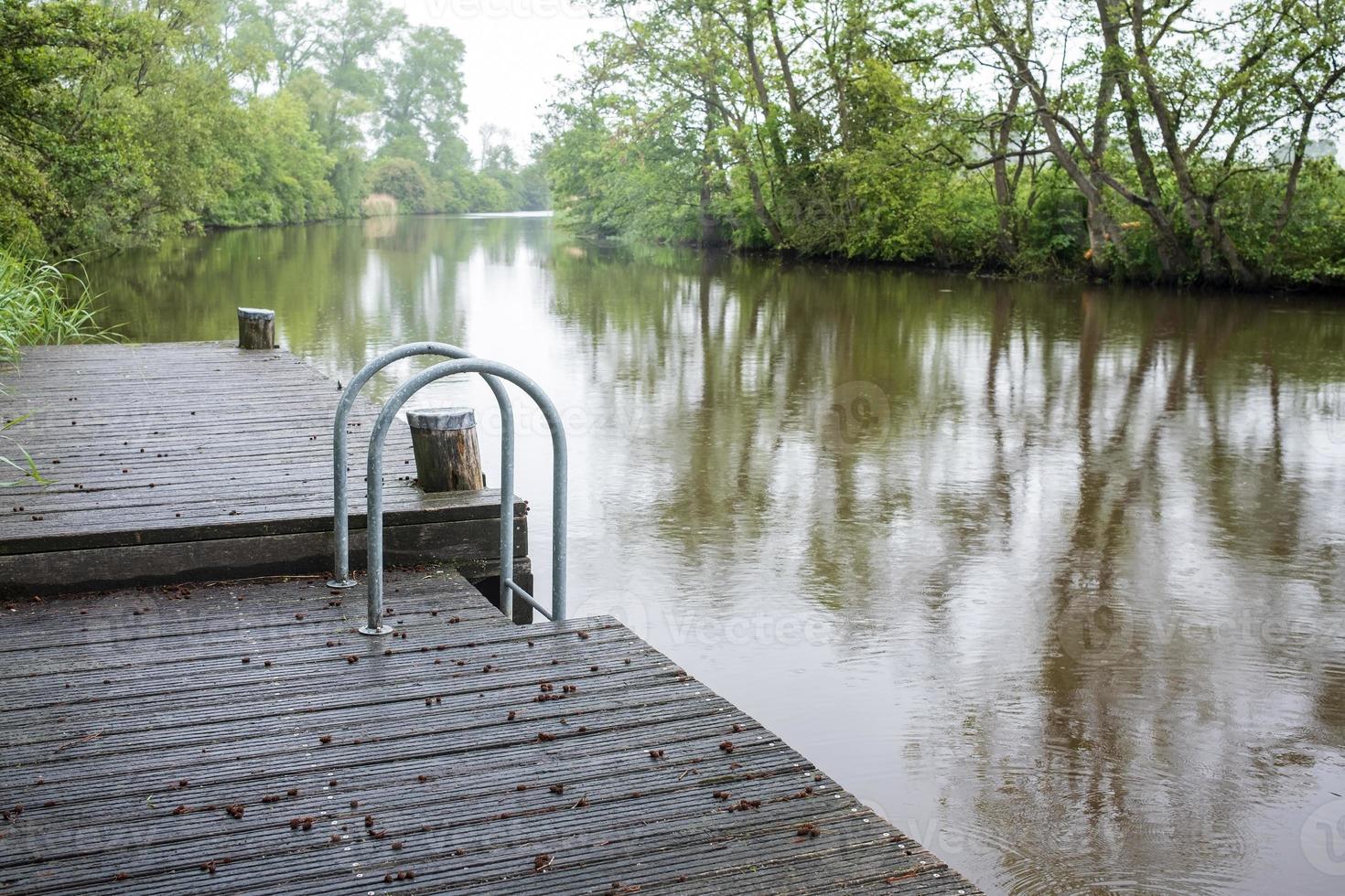 Wooden pier with a metal ladder for easy entry into the water, on the river. Rural landscape. photo