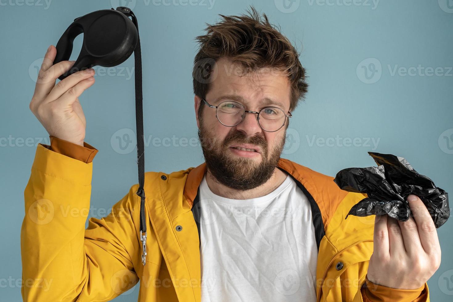 Annoyed man holds a leash in one hand and a dog poop bag in the other. Squeamish owner does not want to walk with his pet. photo