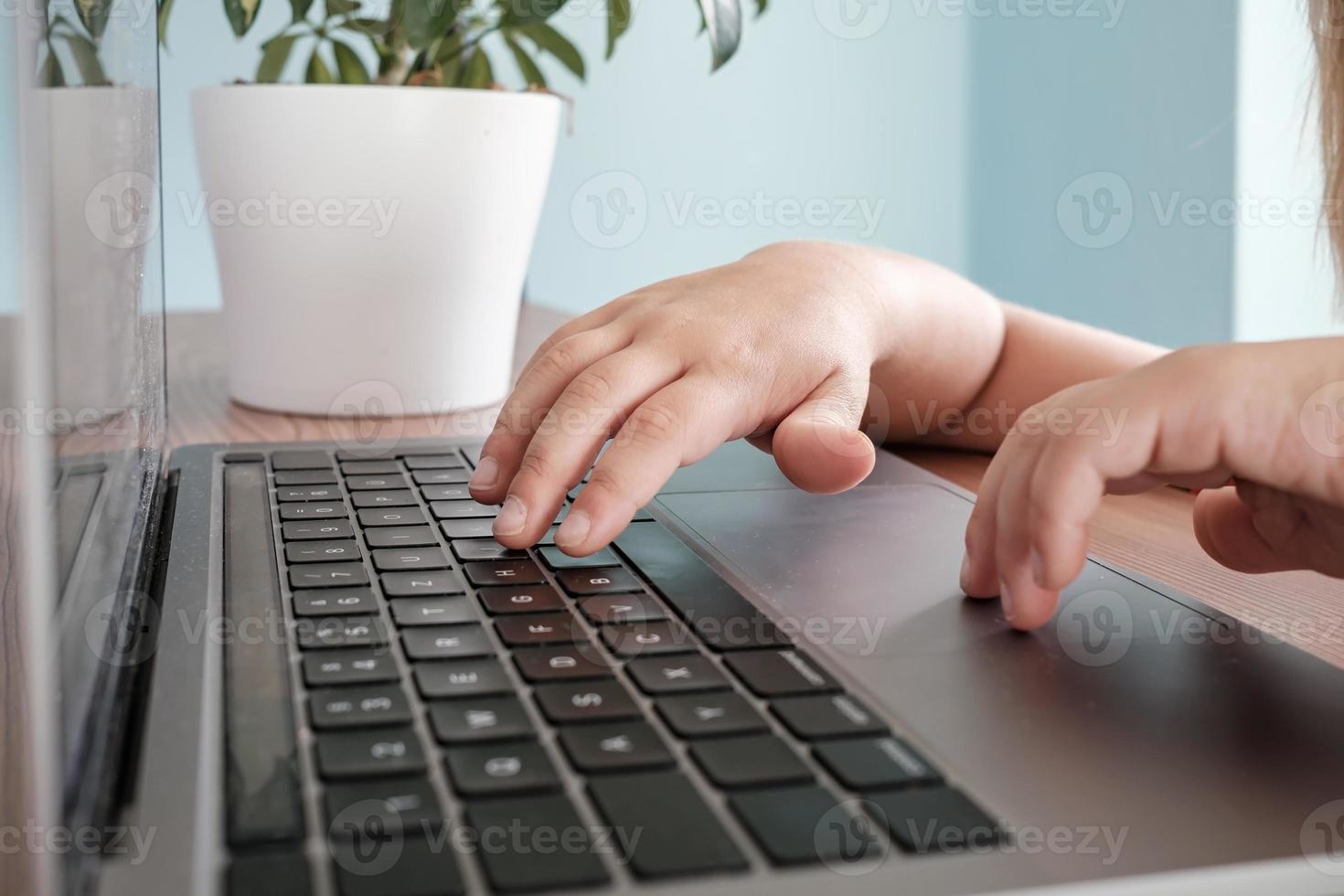 children's hands typing on laptop keyboard on table photo