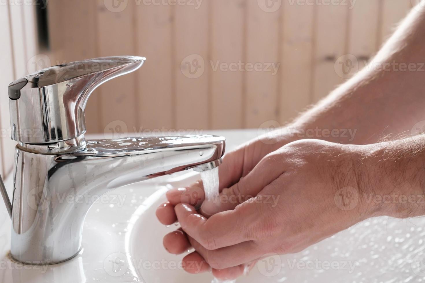 Man washes hands under a stream of clean running water, over the sink