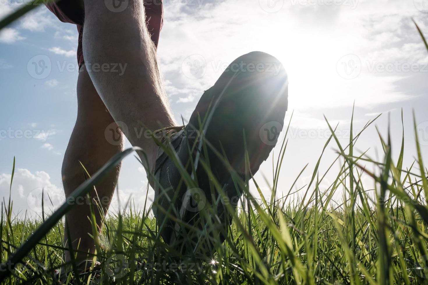 Foot in sneakers walks along a meadow, against the backdrop of the sun and sky. Active lifestyle and vacation concept. Bottom view. photo