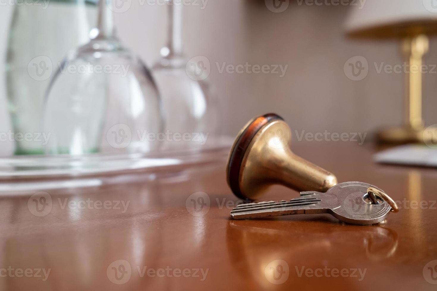 Key with a key fob from the hotel room lies on the table, against a blurred background of clean wine glasses and a lamp. Close-up. photo