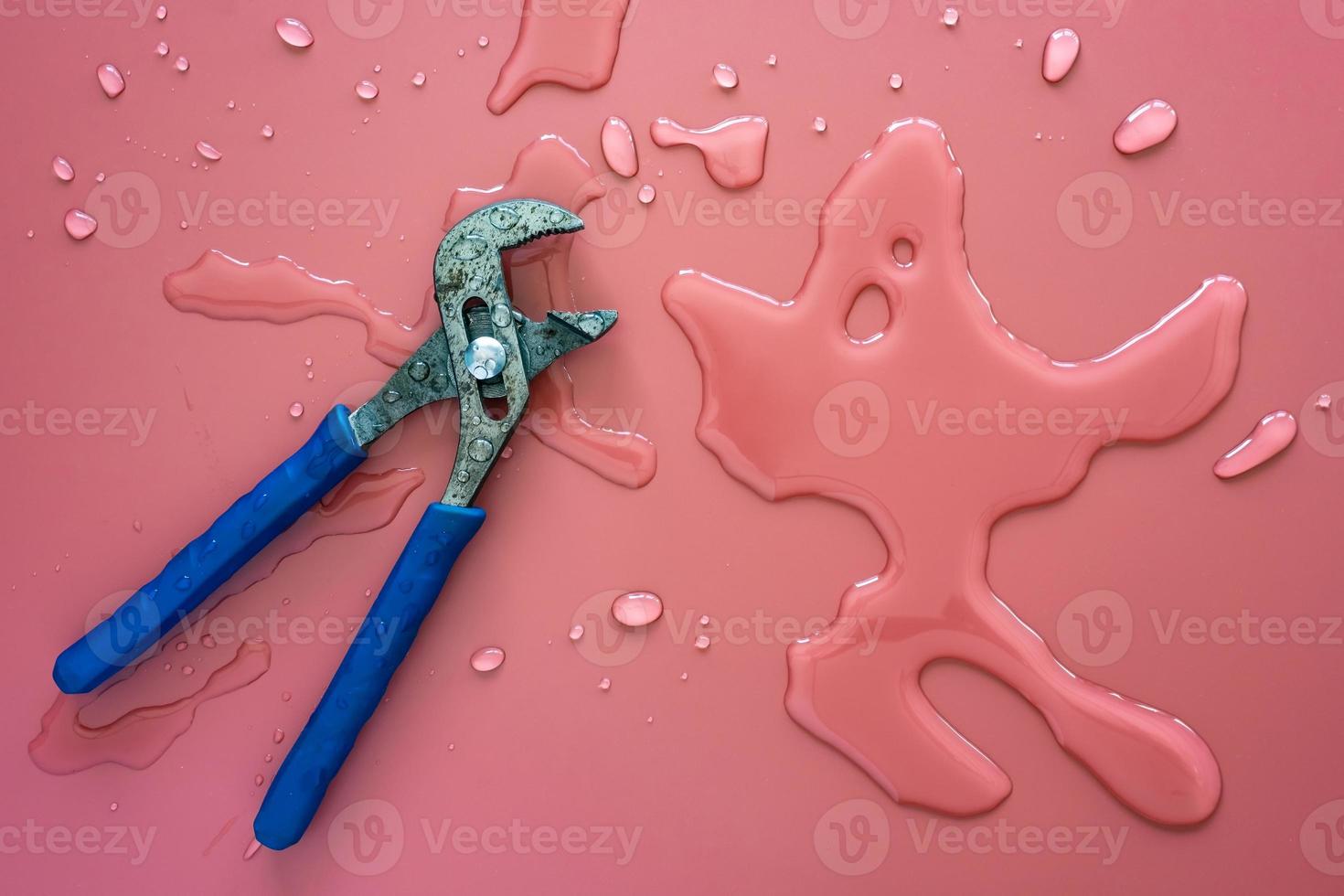 Wrench for plumbing lies on a pink background and spilled clean water. Copy space. Top view. photo