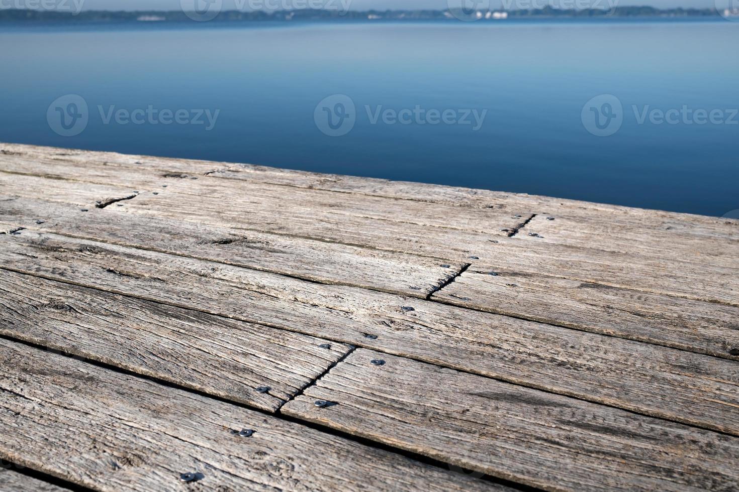 Old wooden pier made of weathered boards with nails, against the backdrop of a lake. Copy space. photo