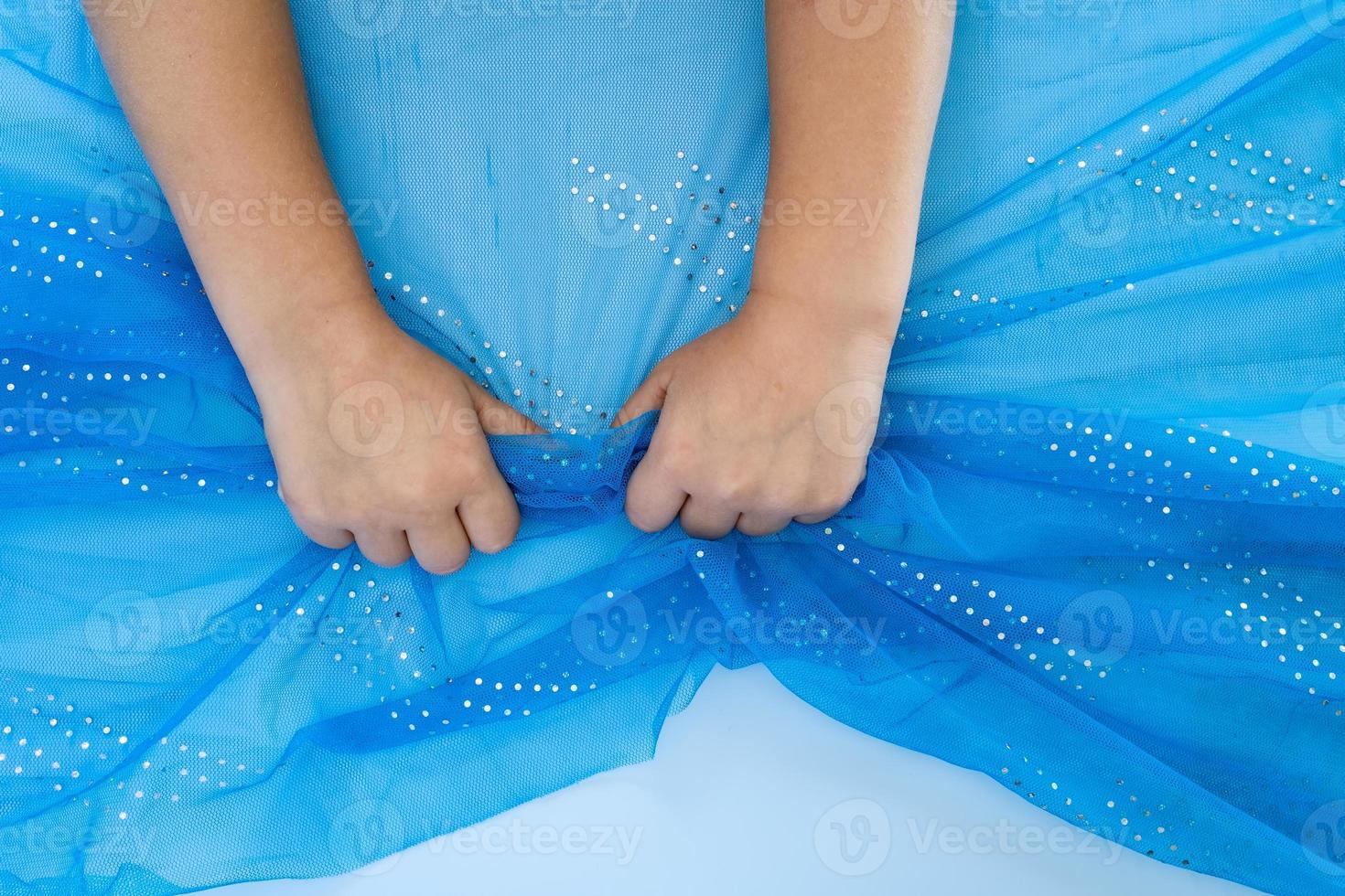 Children hands clench in fists the edge of a blue transparent fabric with a silvery pattern on a white background. Copy space. photo