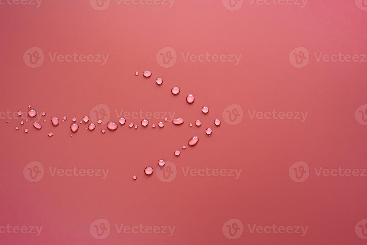 Arrow from drops of pure water, on a pink background. Sign showing the way. Copy space. Top view. photo