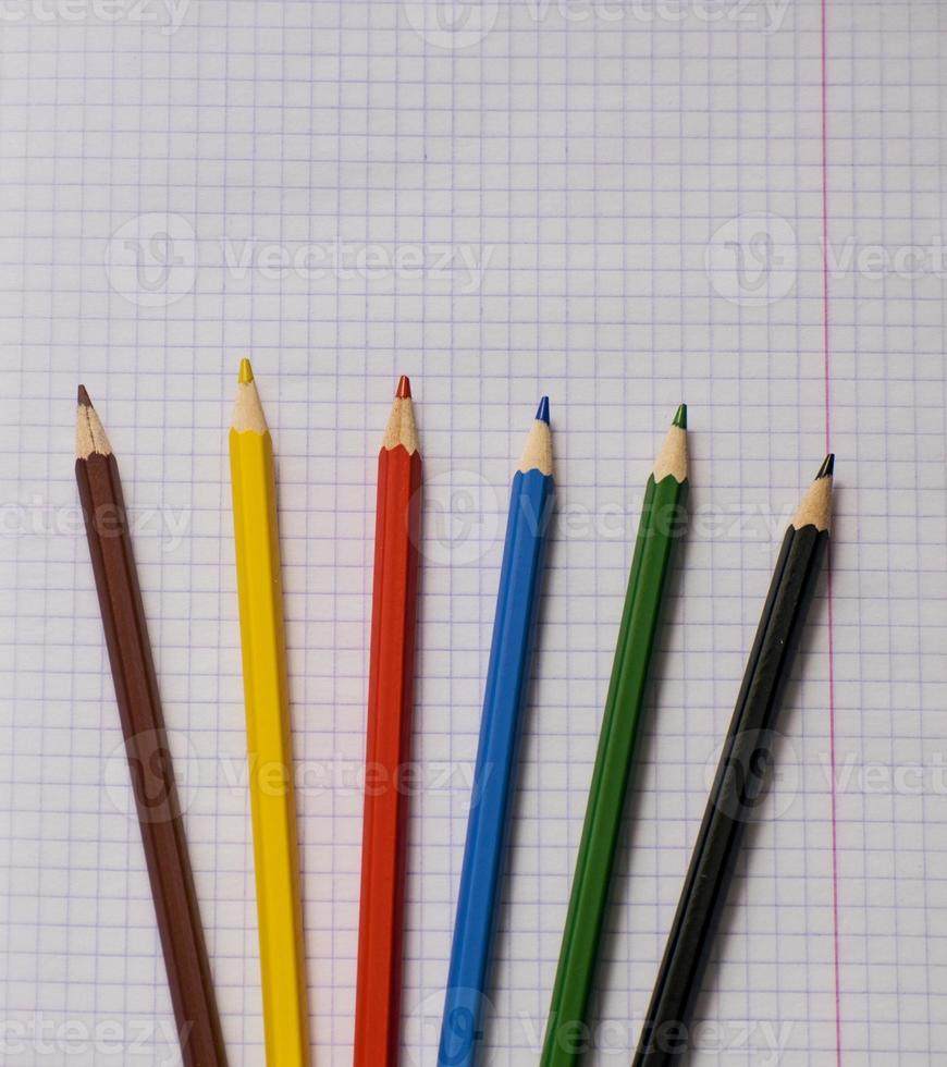 Blank paper and colorful pencils. Colored pencils on a notebook sheet. School notebook. View from above. photo